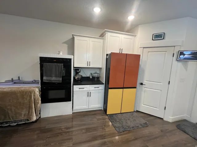 Kitchen with white cabinets, dark countertops, dark wood-style flooring, and freestanding refrigerator