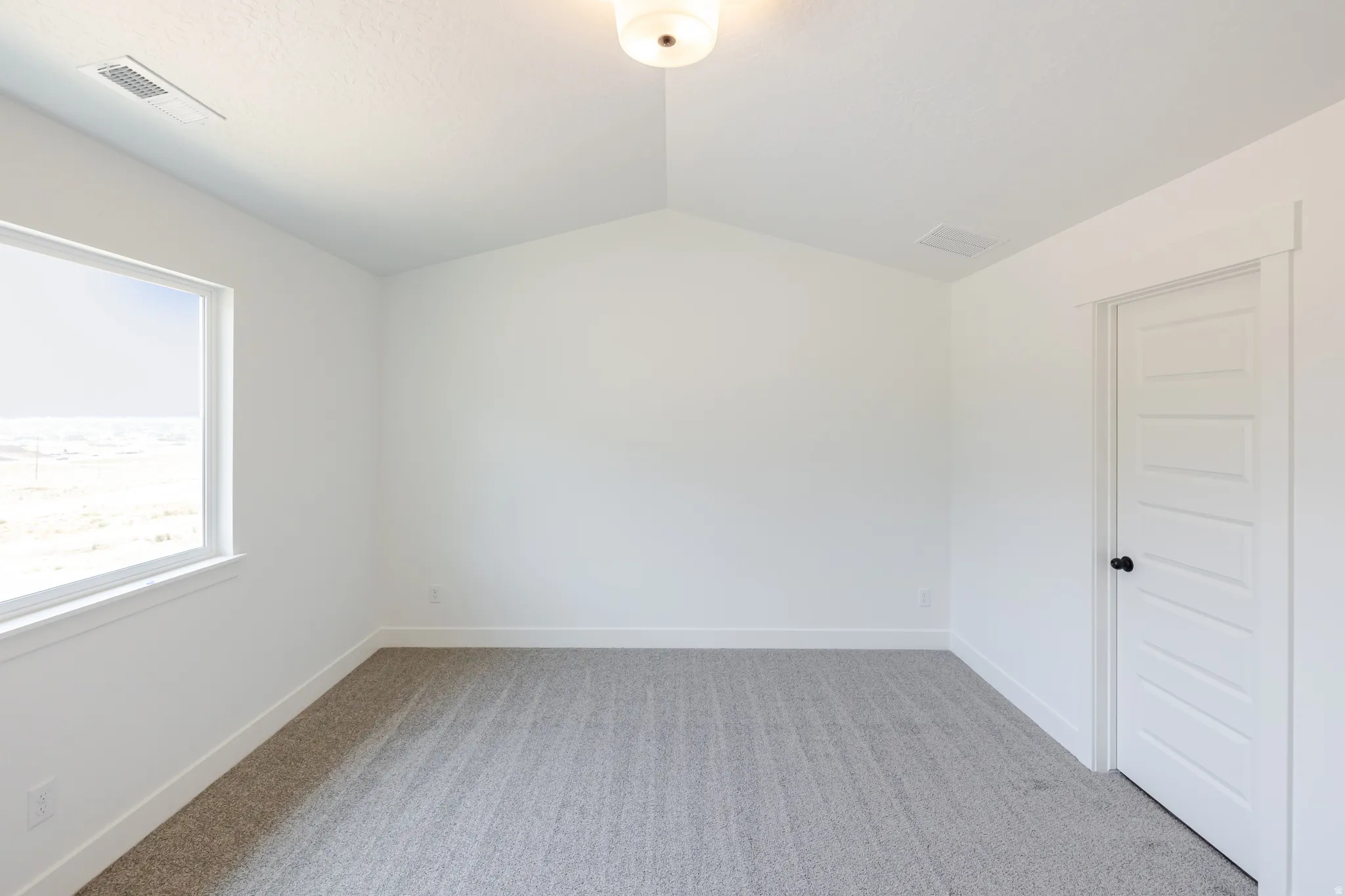 Bright room featuring a vaulted ceiling and light gray carpet