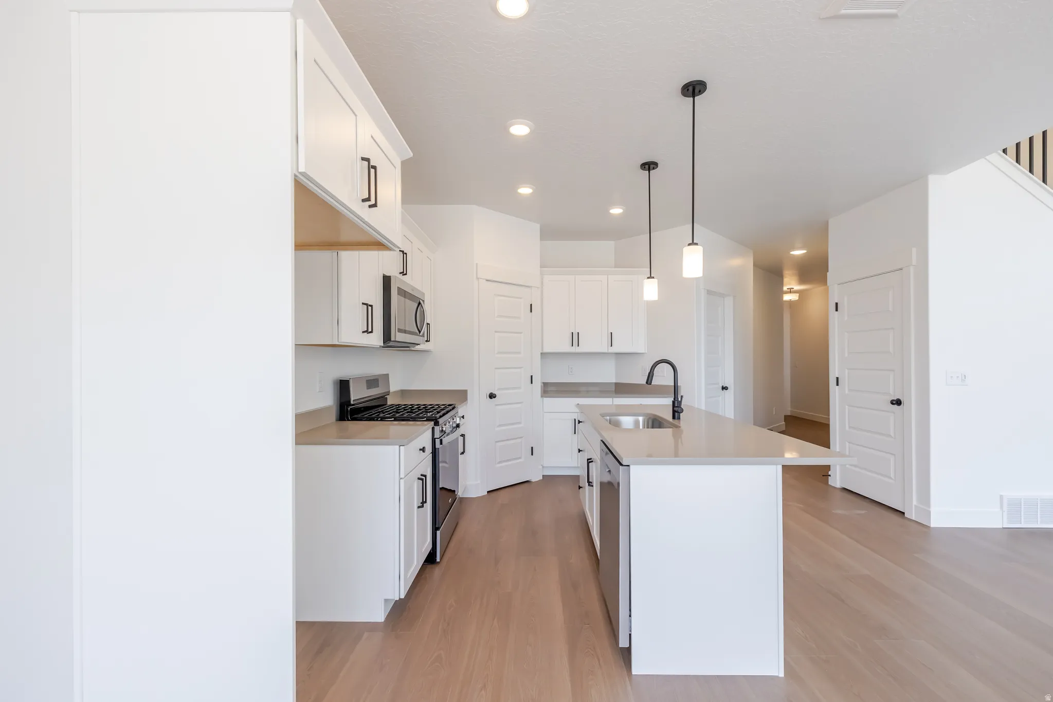 Open-concept kitchen featuring white cabinetry, stainless steel appliances, a central island with an undermount sink, and pendant lighting