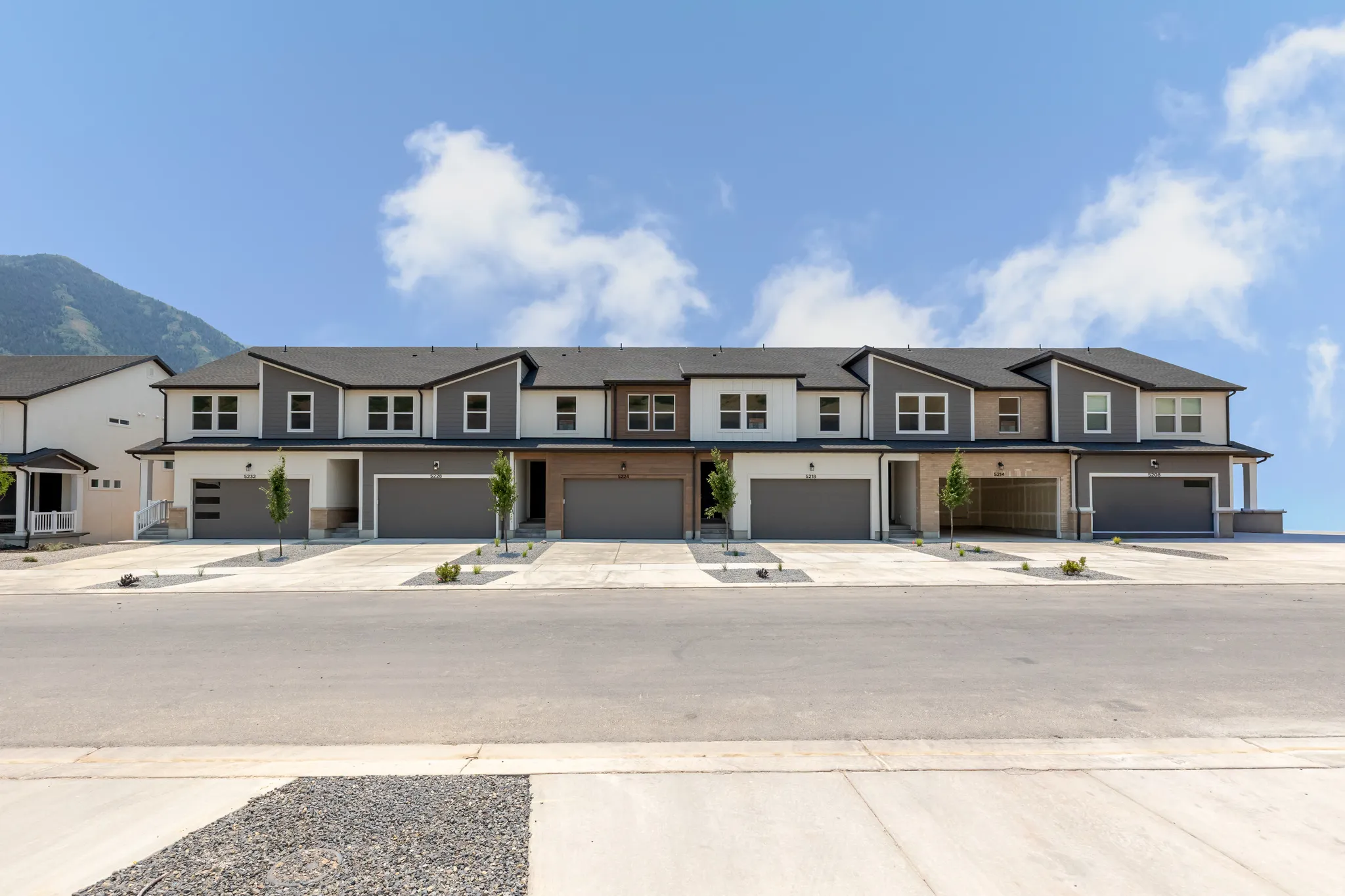 Modern townhome community featuring a mountain backdrop, a combination of smooth and textured exterior siding, attached garages with contemporary doors, and individual paved driveways