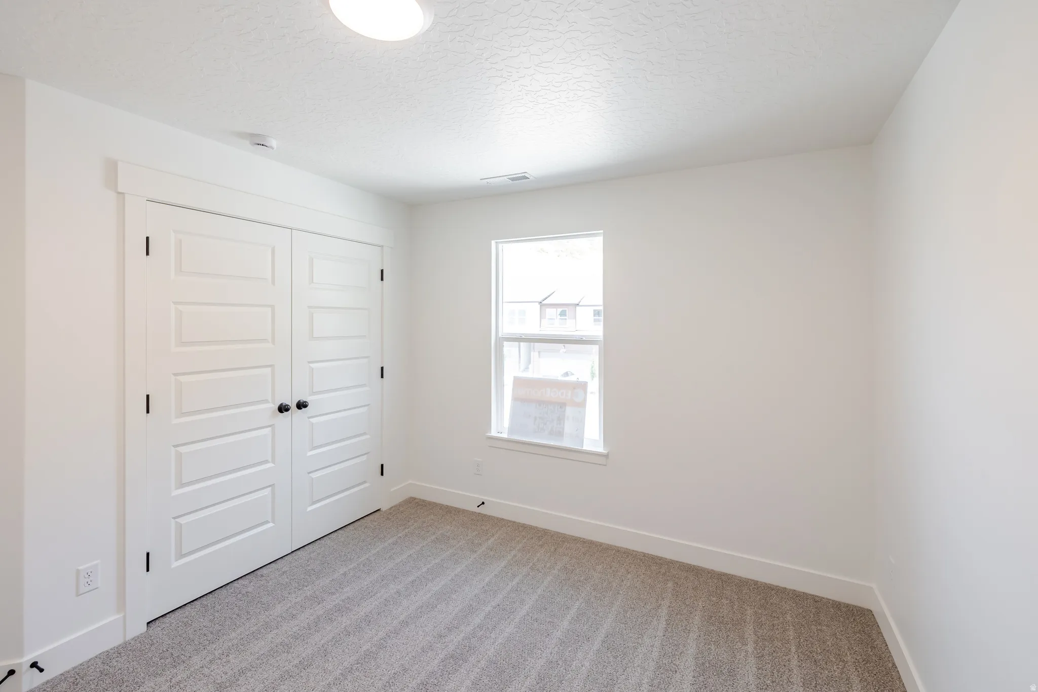 Bedroom featuring neutral-toned carpet, a single window, and bi-fold closet doors with black hardware