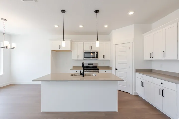 Kitchen featuring a central island with an undermount sink, white cabinetry with matte black hardware, stainless steel appliances, and recessed lighting