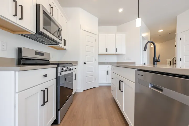 Modern kitchen featuring white shaker cabinetry, stainless steel appliances, solid surface countertops, a matte black faucet, and wood-finish flooring