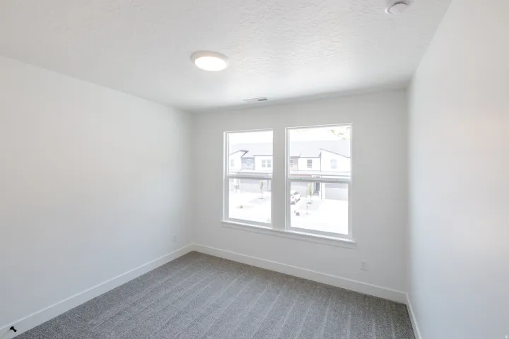 Bright room featuring two large windows, white walls, gray patterned carpet, white baseboards, and a flush-mount ceiling light
