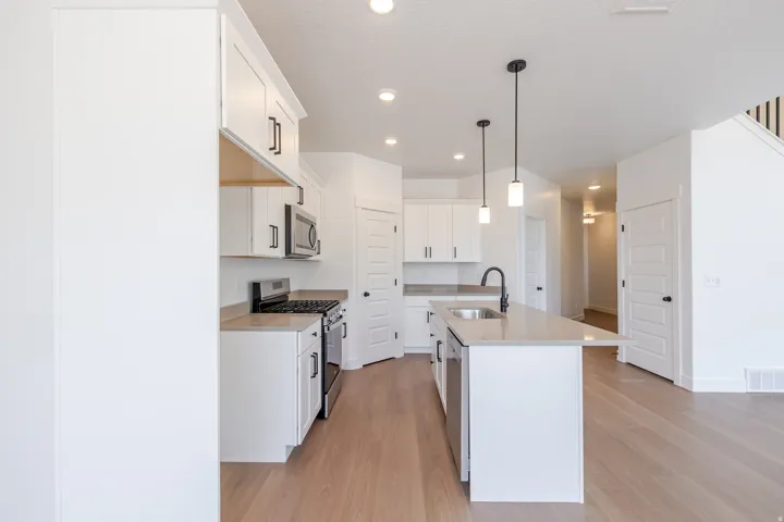 Open-concept kitchen featuring white cabinetry, stainless steel appliances, a central island with an undermount sink, and pendant lighting
