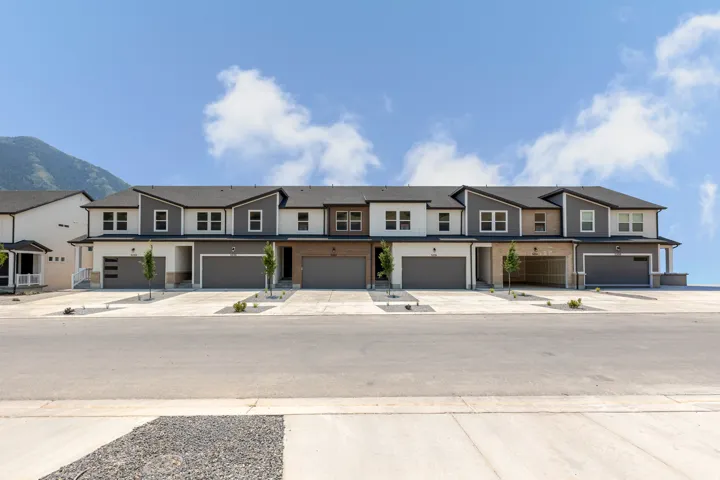 Modern townhome community featuring a mountain backdrop, a combination of smooth and textured exterior siding, attached garages with contemporary doors, and individual paved driveways