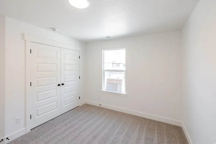 Bedroom featuring neutral-toned carpet, a single window, and bi-fold closet doors with black hardware