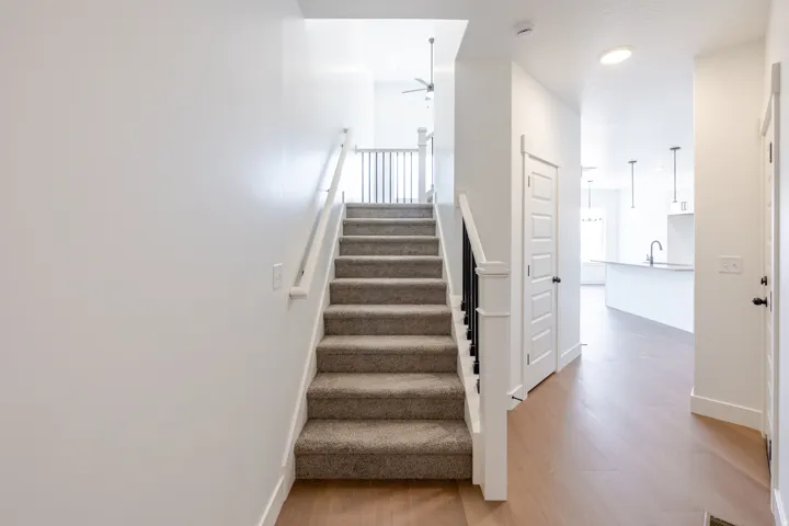 Carpeted staircase with white and black balustrade, wood-finish flooring, and recessed lighting