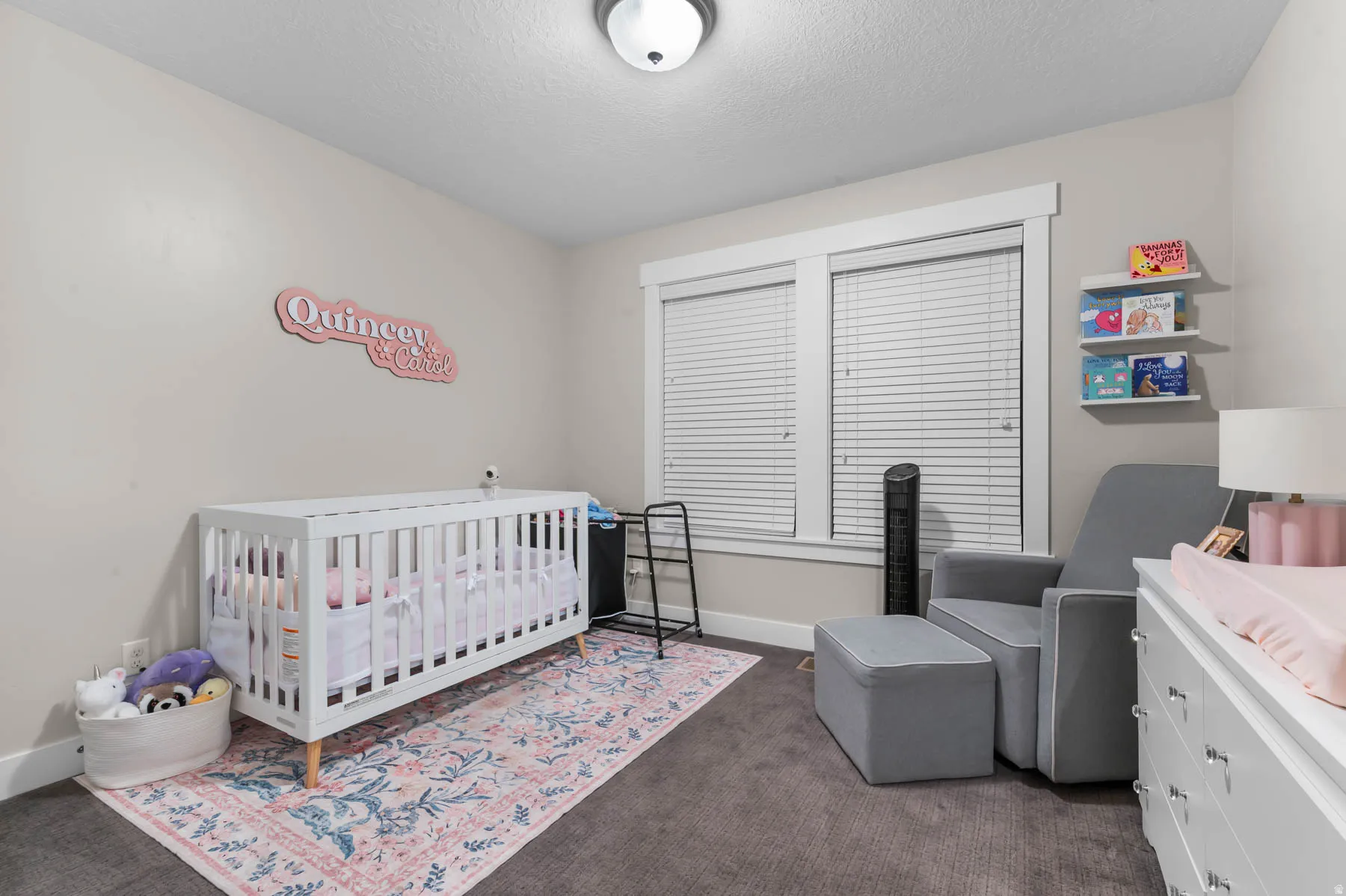 Bedroom featuring a nursery area, dark colored carpet, and a textured ceiling