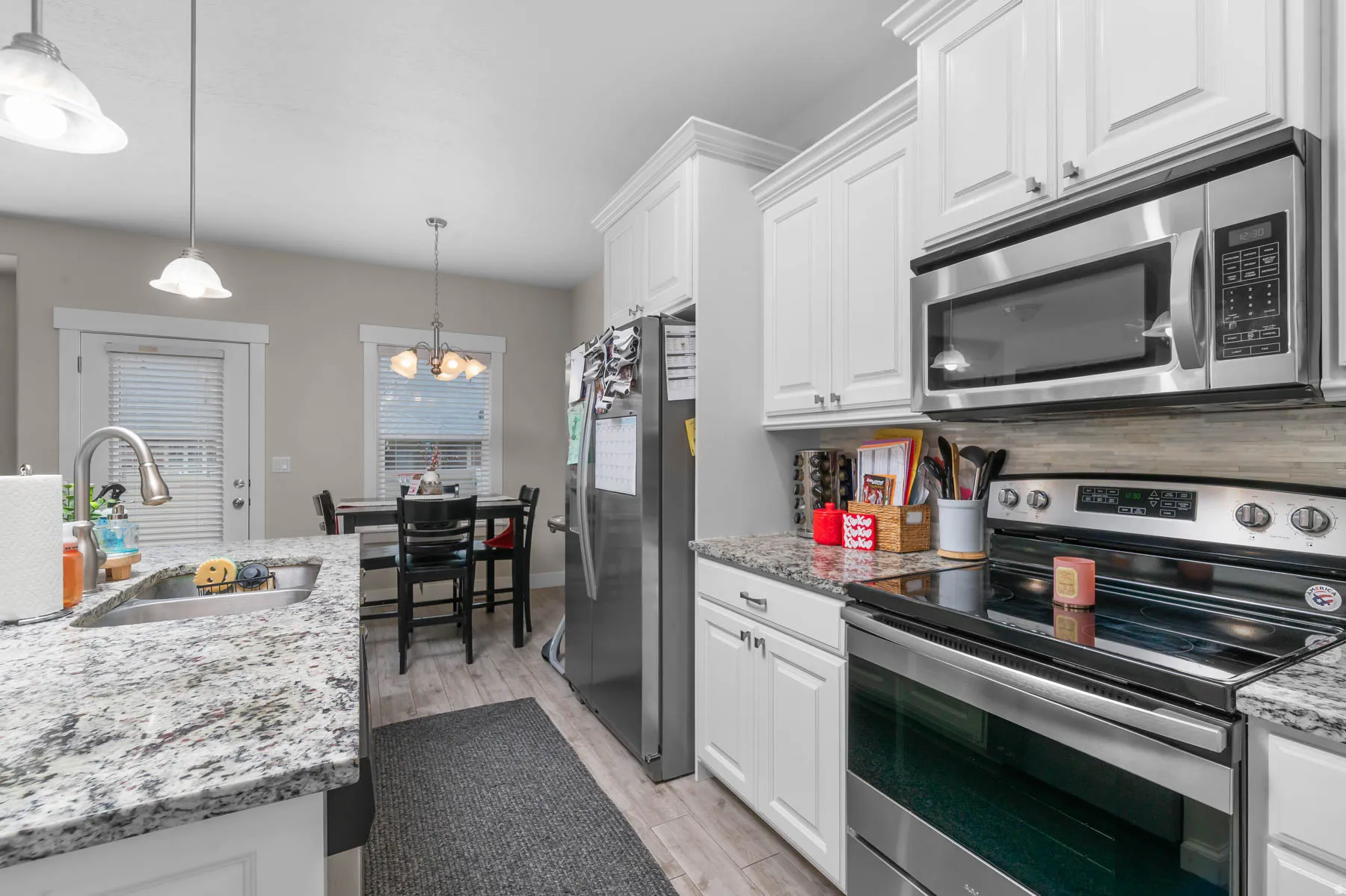 Kitchen with stainless steel appliances, light stone countertops, white cabinets, and light wood-style flooring