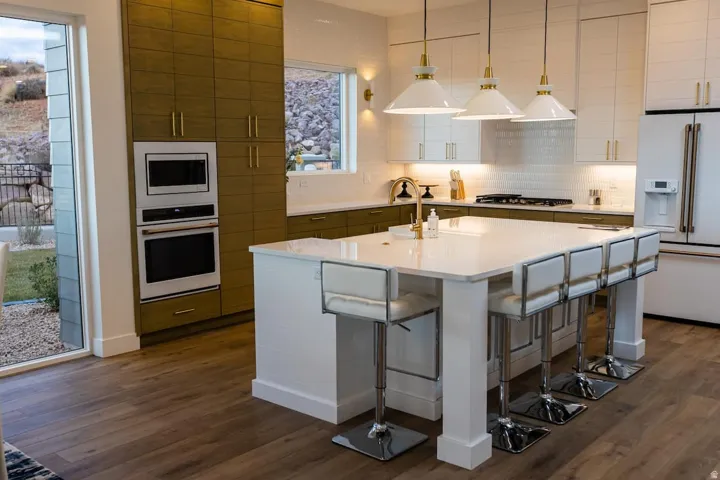 Dual tone kitchen with pendant lighting, stainless steel appliances, a breakfast bar, a kitchen island with sink, and dark wood-type flooring