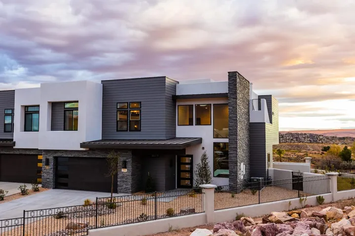 Contemporary home with a fenced front yard, concrete driveway, stone siding, a standing seam roof, and a garage