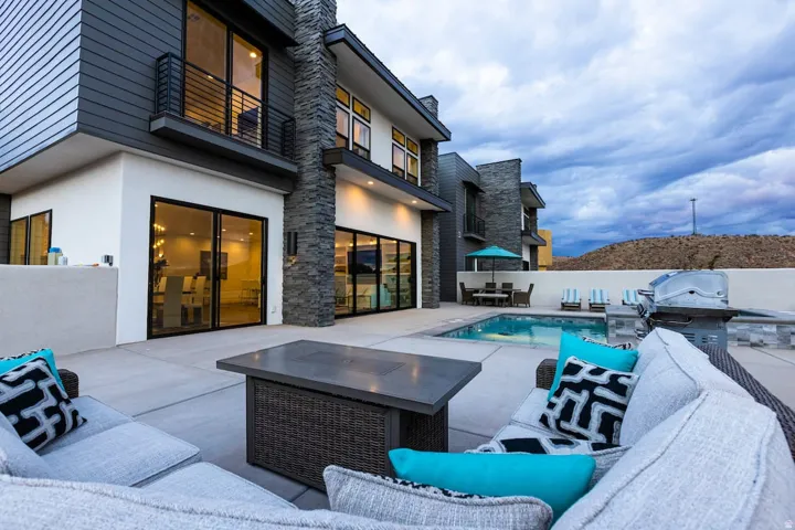 View of swimming pool with a balcony, patio surround, an outdoor kitchen, and an outdoor living / dining area