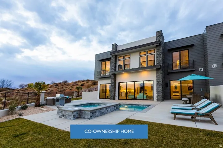Back of property with stone siding, a balcony, a patio, and a pool with connected hot tub