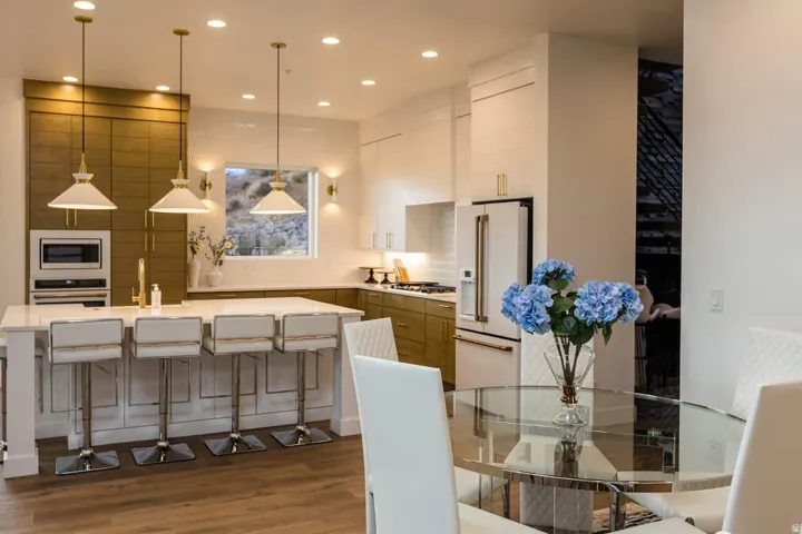 Dual tone kitchen featuring a kitchen bar, two tone cabinetry, stainless steel appliances, dark wood finished floors, and hanging light fixtures