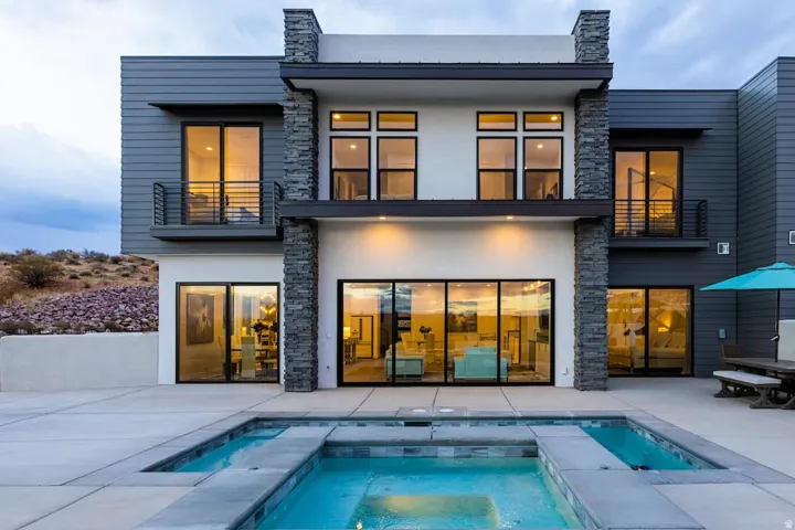 Back of house featuring stone siding, an in-ground hot tub, a balcony, stucco siding, and a patio area