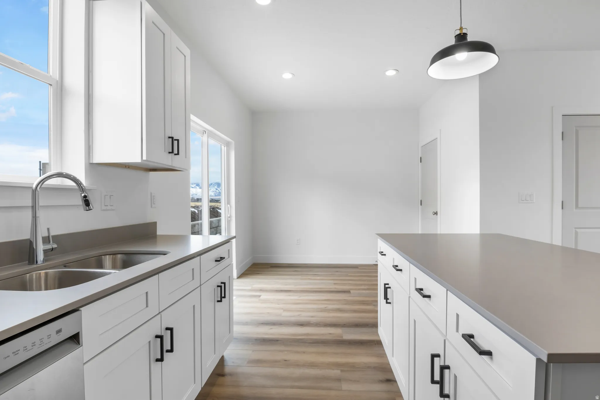 Kitchen with white cabinetry, stainless steel dishwasher, light wood-style flooring, and pendant lighting