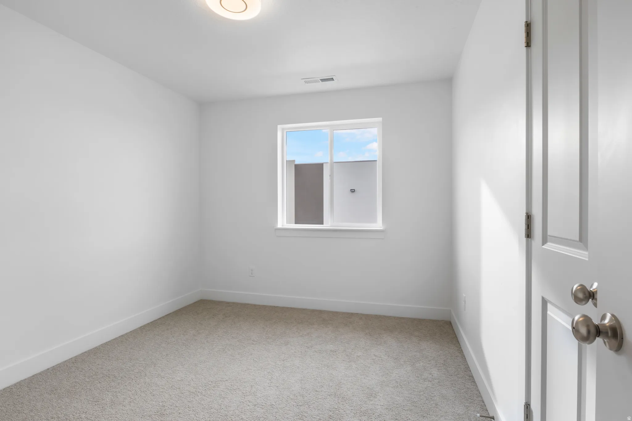 Empty room with light colored carpet and baseboards