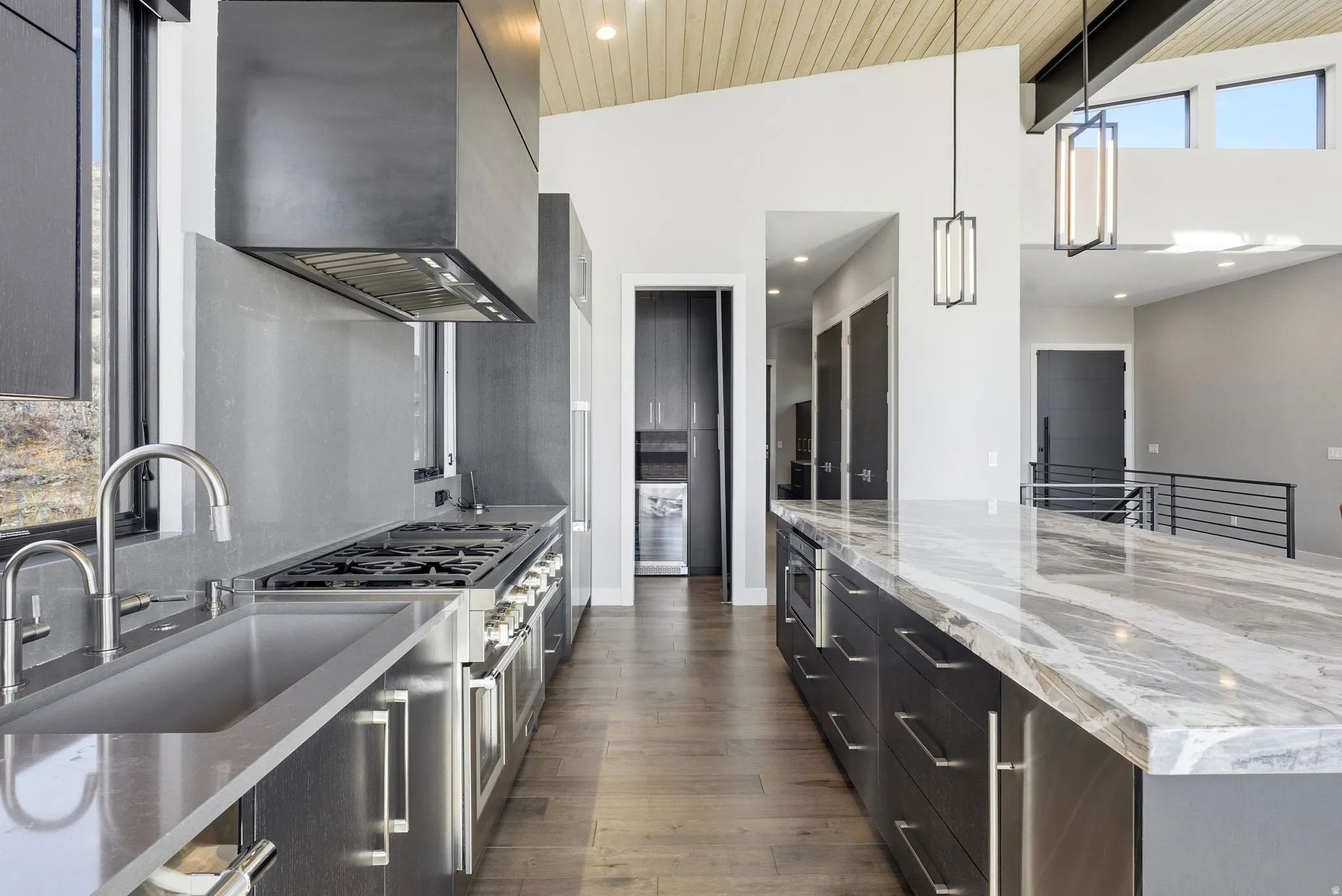 Kitchen with hanging light fixtures, light stone counters, exhaust hood, range with two ovens, and a high wooden beamed ceiling