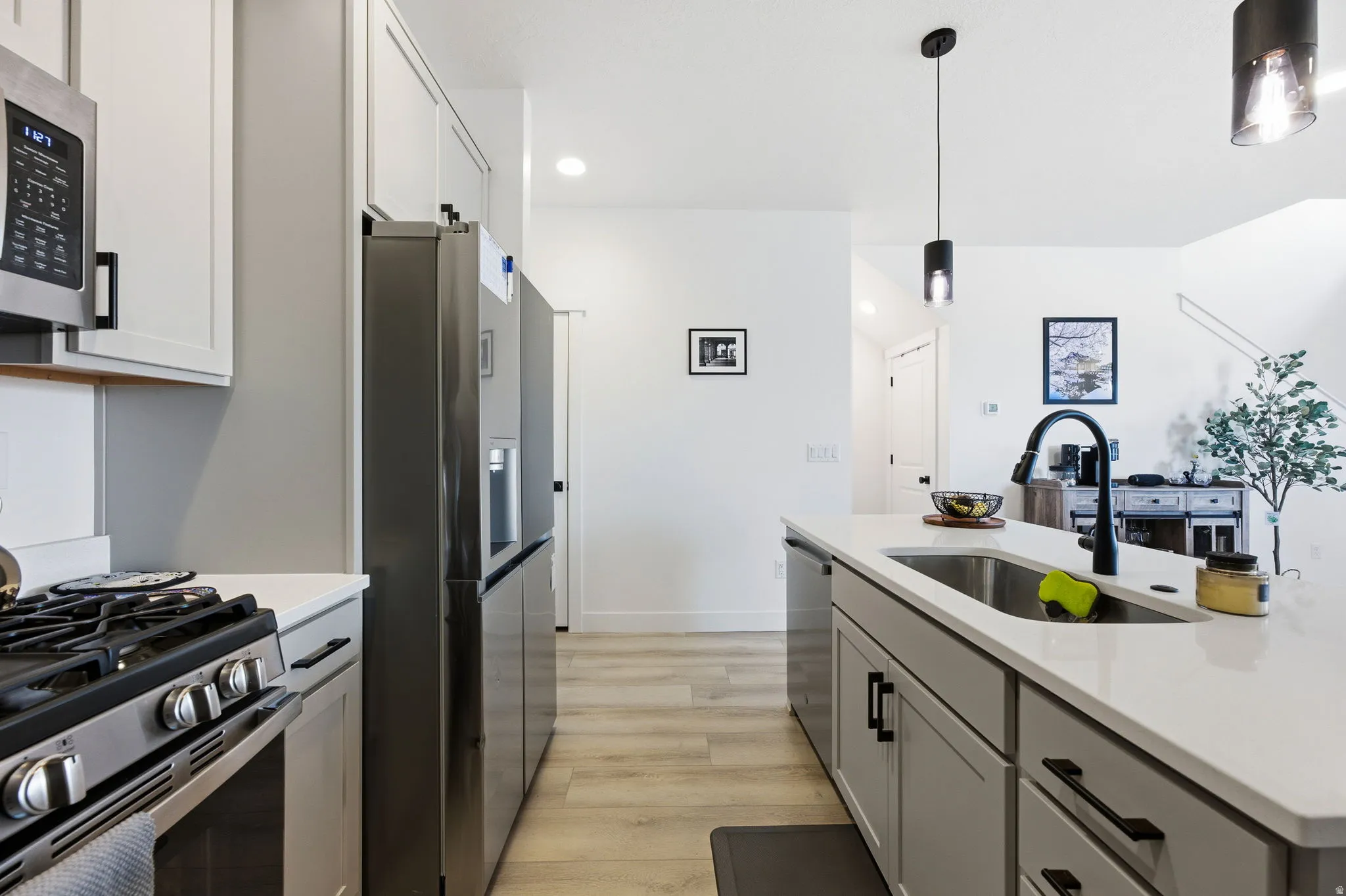 Kitchen featuring stainless steel appliances, light wood-style flooring, decorative light fixtures, light stone countertops, and a center island with sink