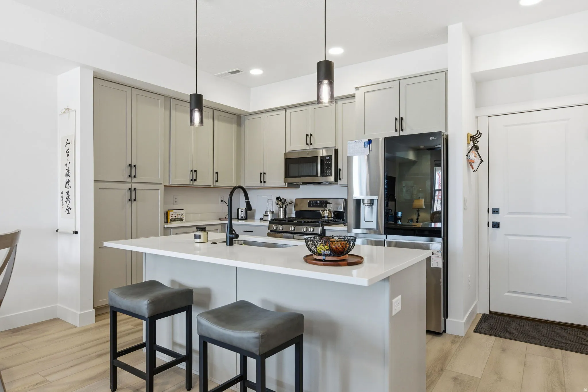 Kitchen with an island with sink, decorative light fixtures, light wood-style floors, a breakfast bar area, and stainless steel appliances
