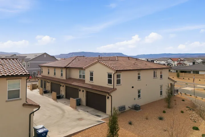 Rear view of house featuring a garage, stucco siding, a residential view, driveway, and a tiled roof