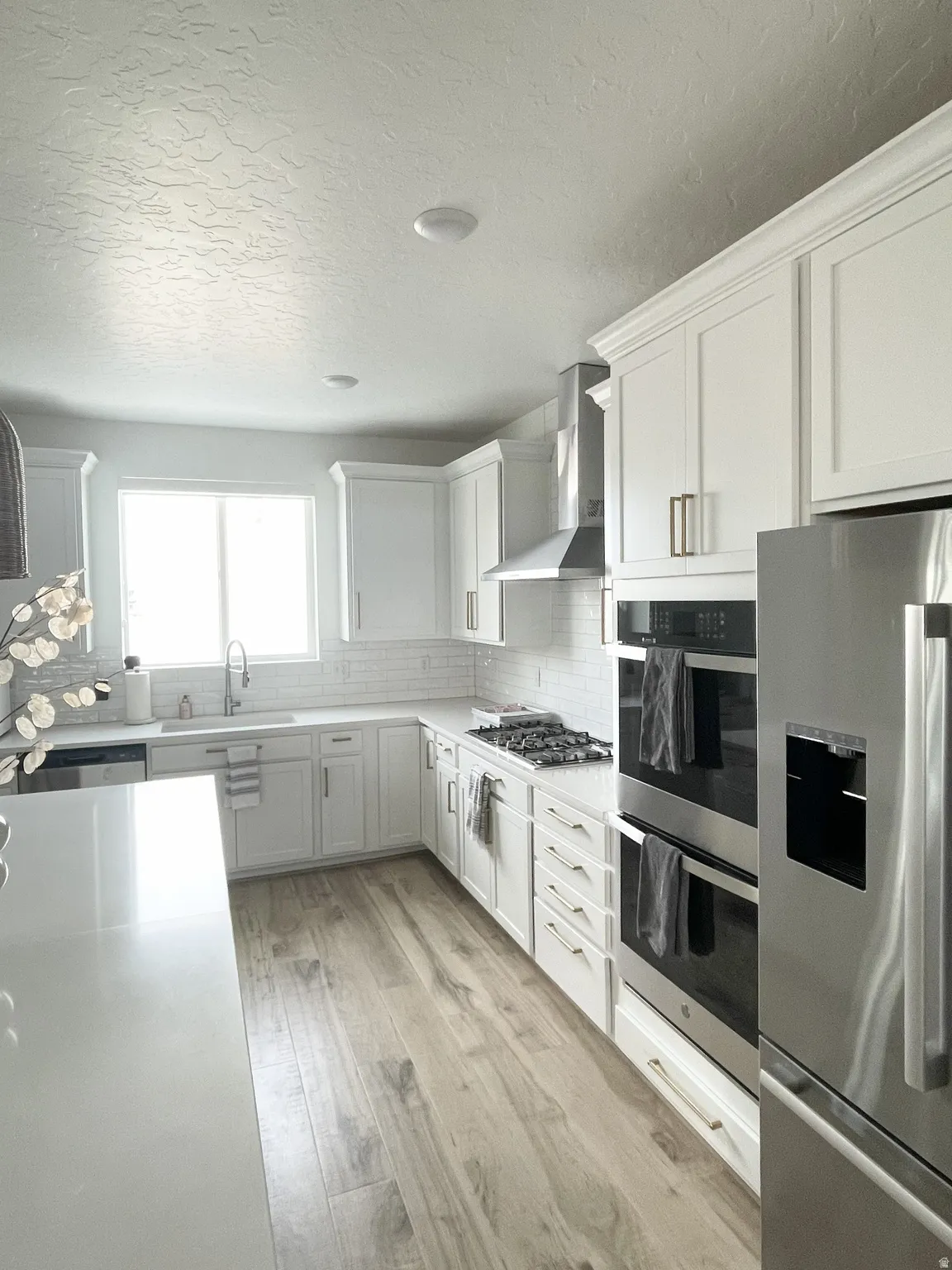 Kitchen featuring stainless steel appliances, backsplash, light wood-style floors, a textured ceiling, and white cabinetry