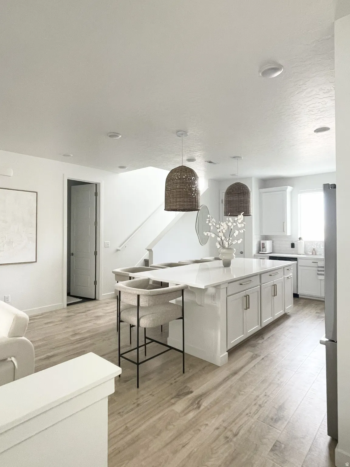 Kitchen with a kitchen island, white cabinets, light wood finished floors, hanging light fixtures, and a kitchen breakfast bar