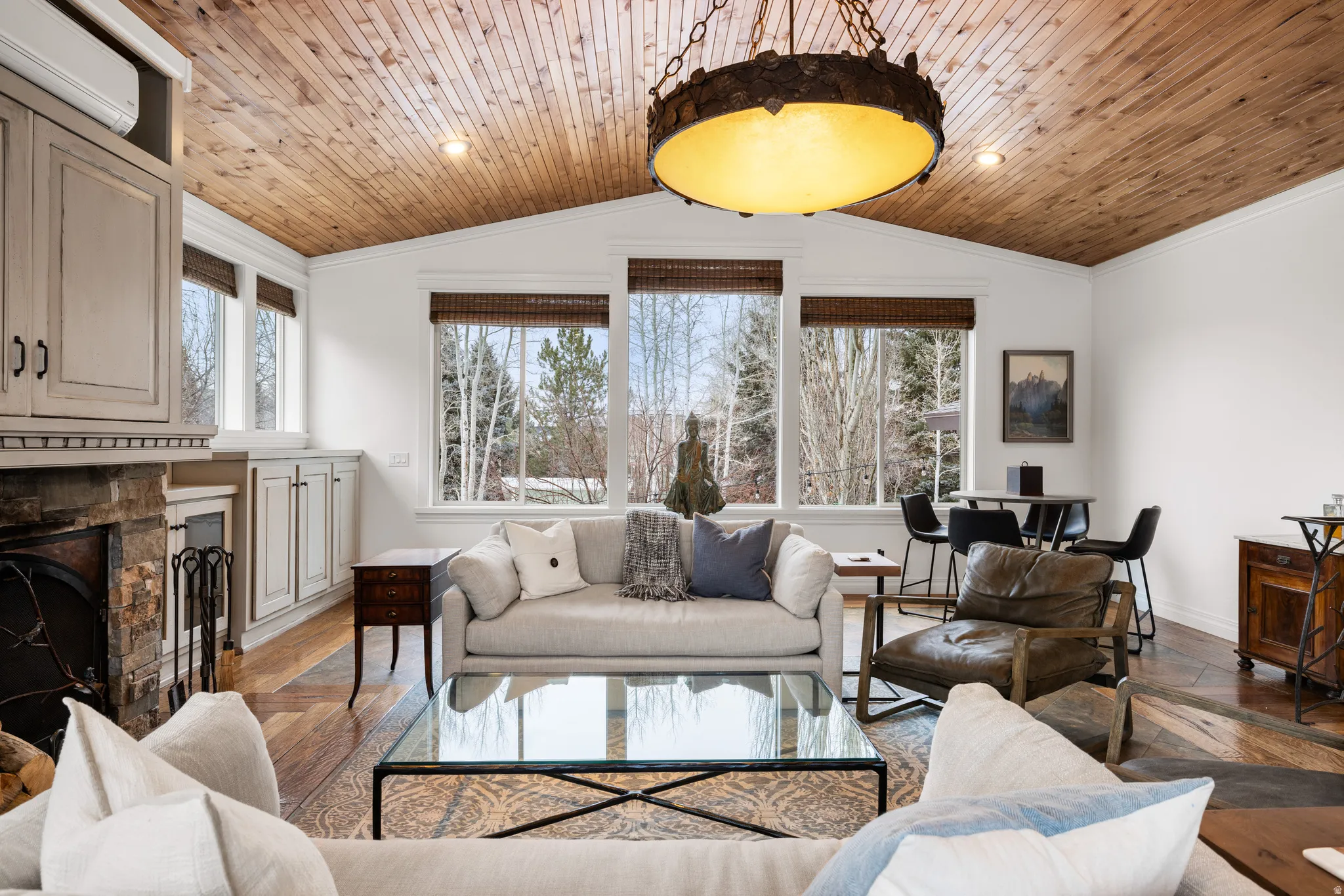 Living room with a stone fireplace, ornamental molding, wooden ceiling, and wood finished floors