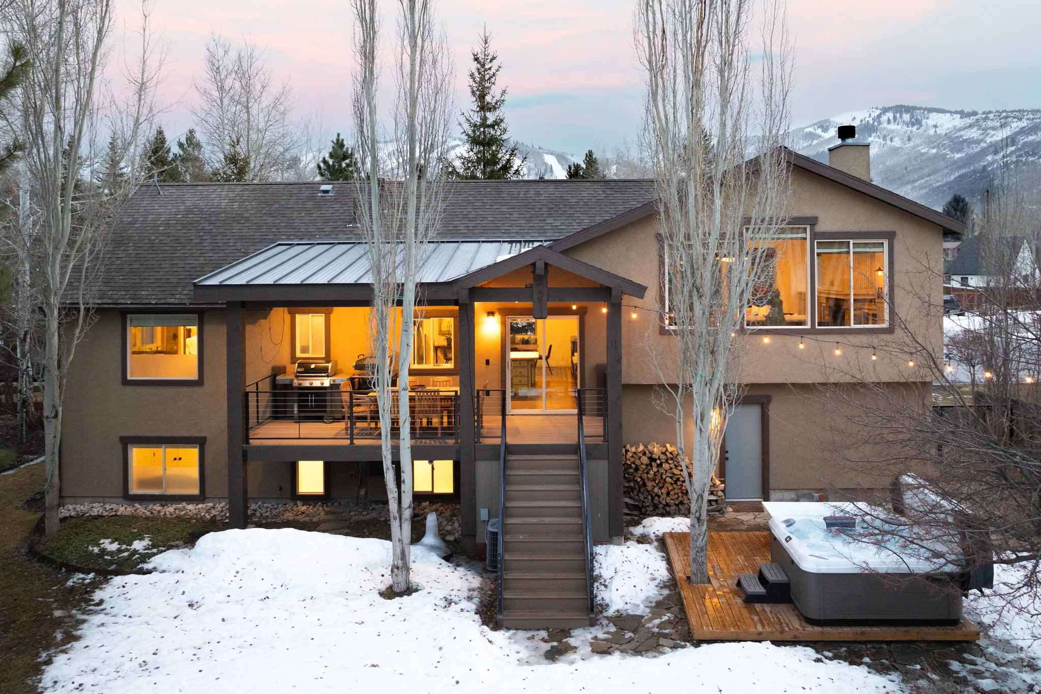 Snow covered rear of property with a deck, a standing seam roof, stucco siding, a shingled roof, and a chimney