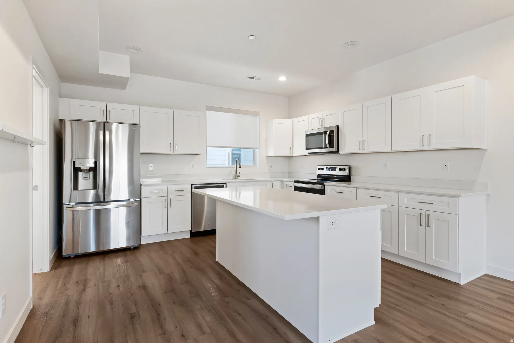 Kitchen featuring white cabinetry, stainless steel appliances, a center island, dark wood-style floors, and recessed lighting