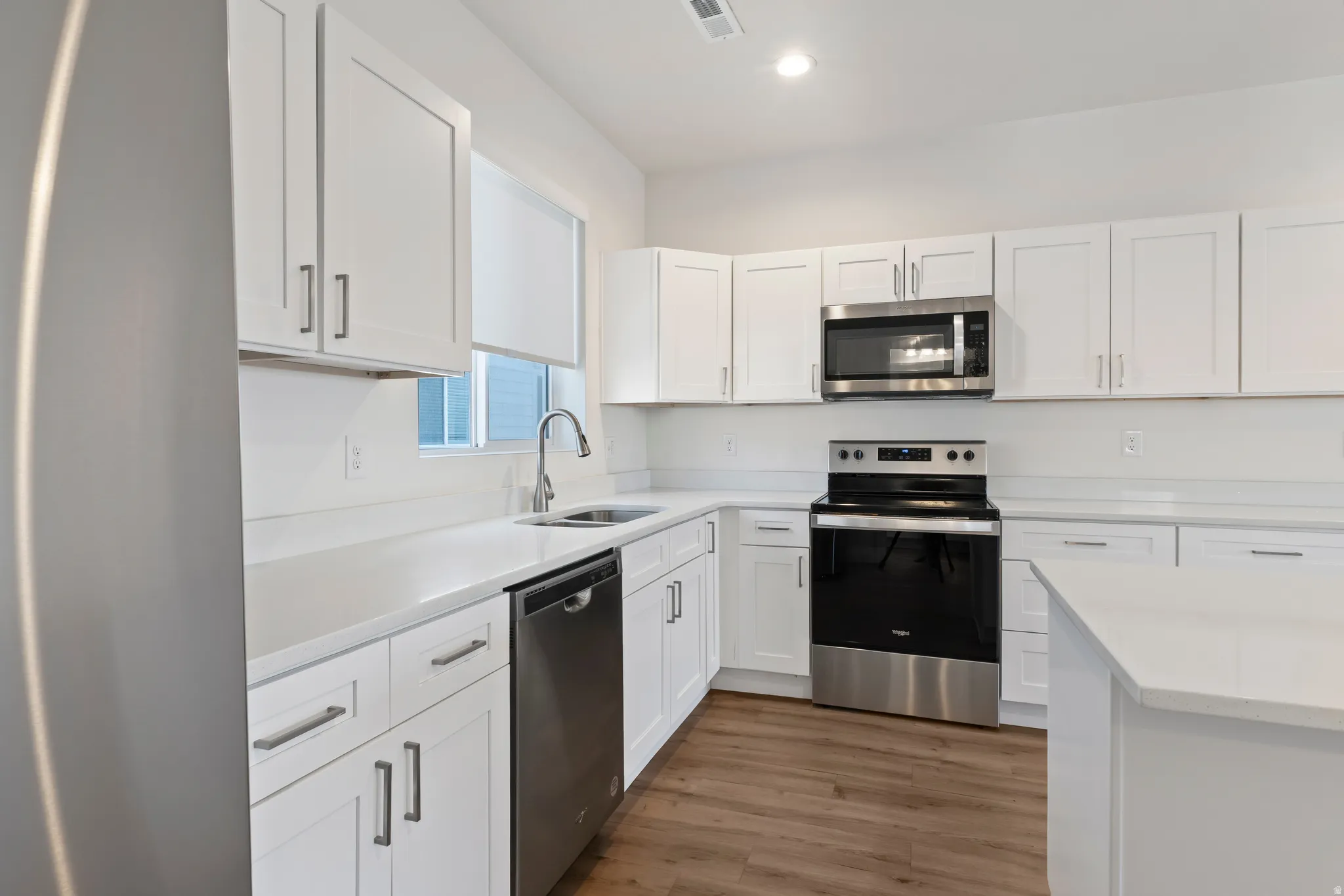 Kitchen featuring stainless steel appliances, white cabinets, dark wood finished floors, light stone counters, and recessed lighting