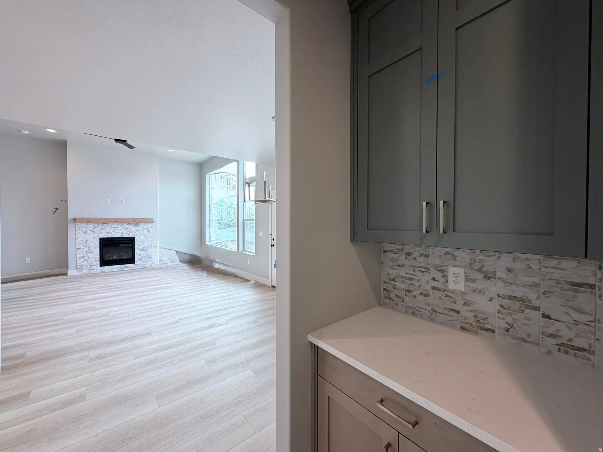 Bar area featuring light wood-type flooring, decorative backsplash, a glass covered fireplace, and light stone countertops
