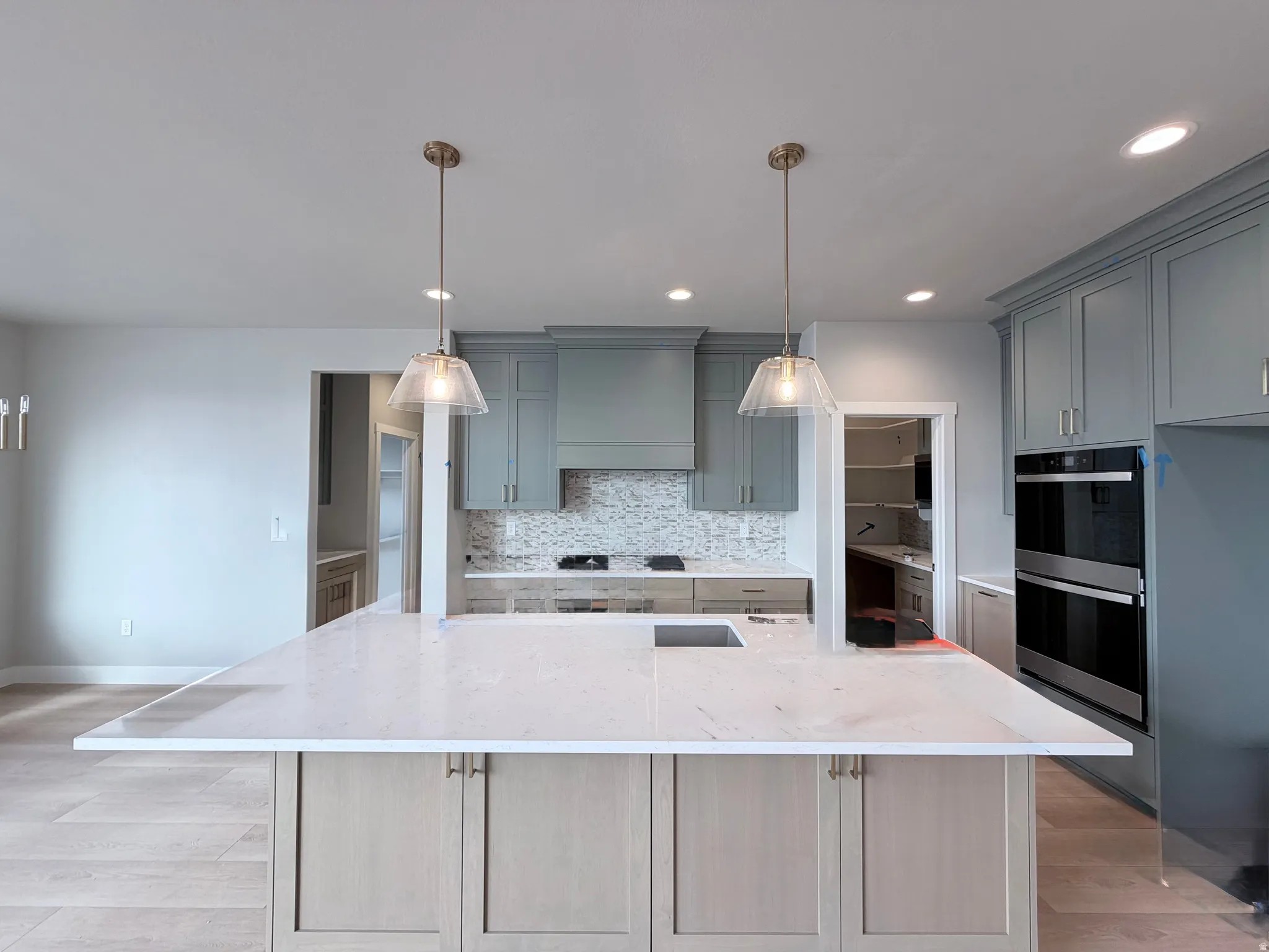 Kitchen with light stone countertops, stainless steel double oven, light wood-style flooring, and gray cabinetry