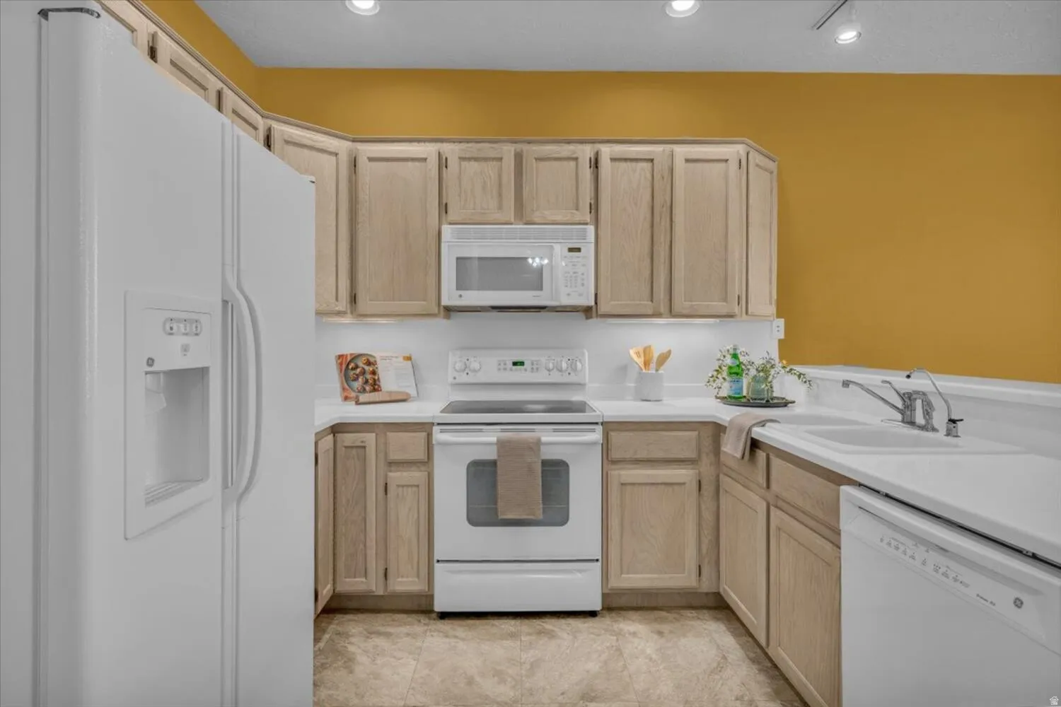 Kitchen featuring light wood finish cabinets, white appliances, and light countertops