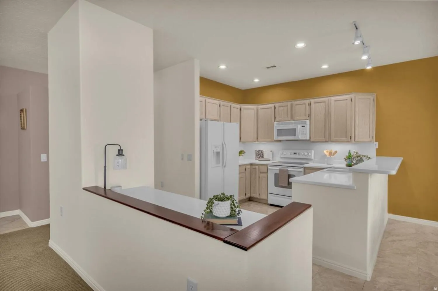 Kitchen with a peninsula, white appliances, recessed lighting, a kitchen bar, and light wood finish cabinetry