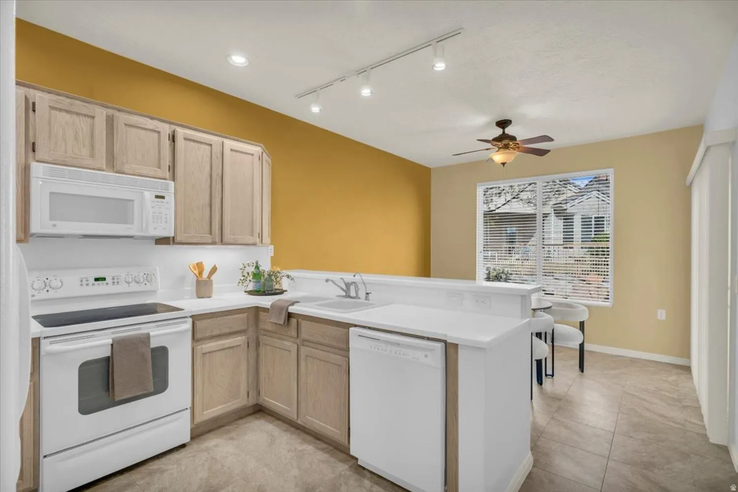 Kitchen with white appliances, light wood finish cabinets, a peninsula, light countertops, and rail lighting