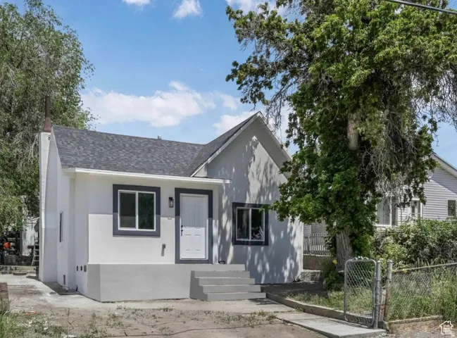 View of front of house with a shingled roof, stucco siding, and a gate