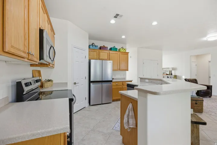 Kitchen featuring stainless steel appliances, an island with sink, light countertops, light tile patterned floors, and recessed lighting