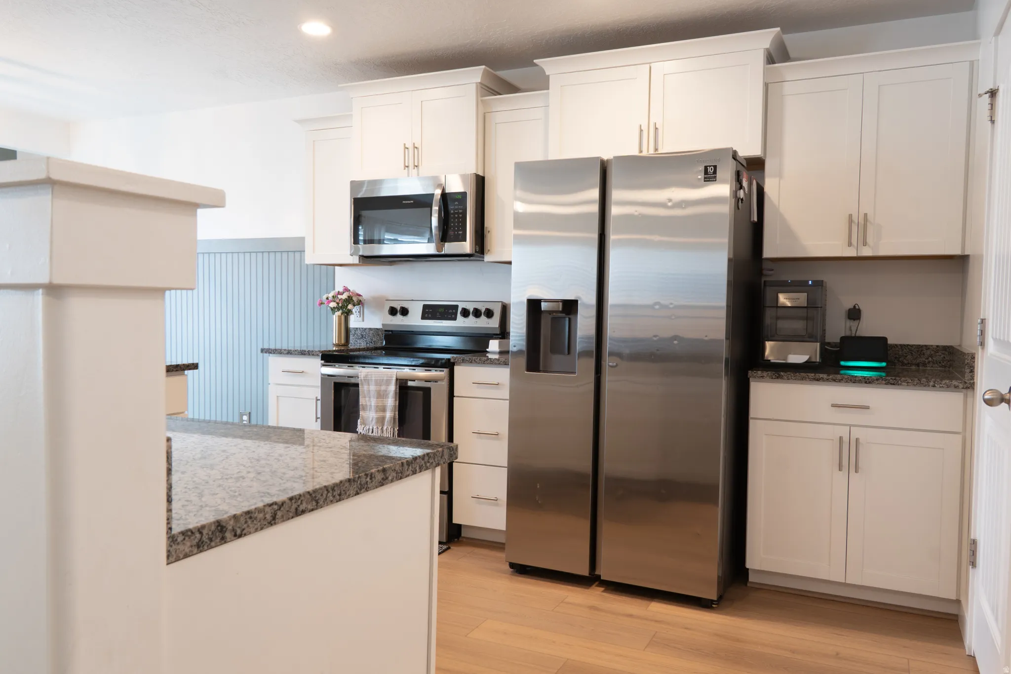 Kitchen featuring stainless steel appliances, light wood-type flooring, white cabinetry, dark stone counters, and wainscoting