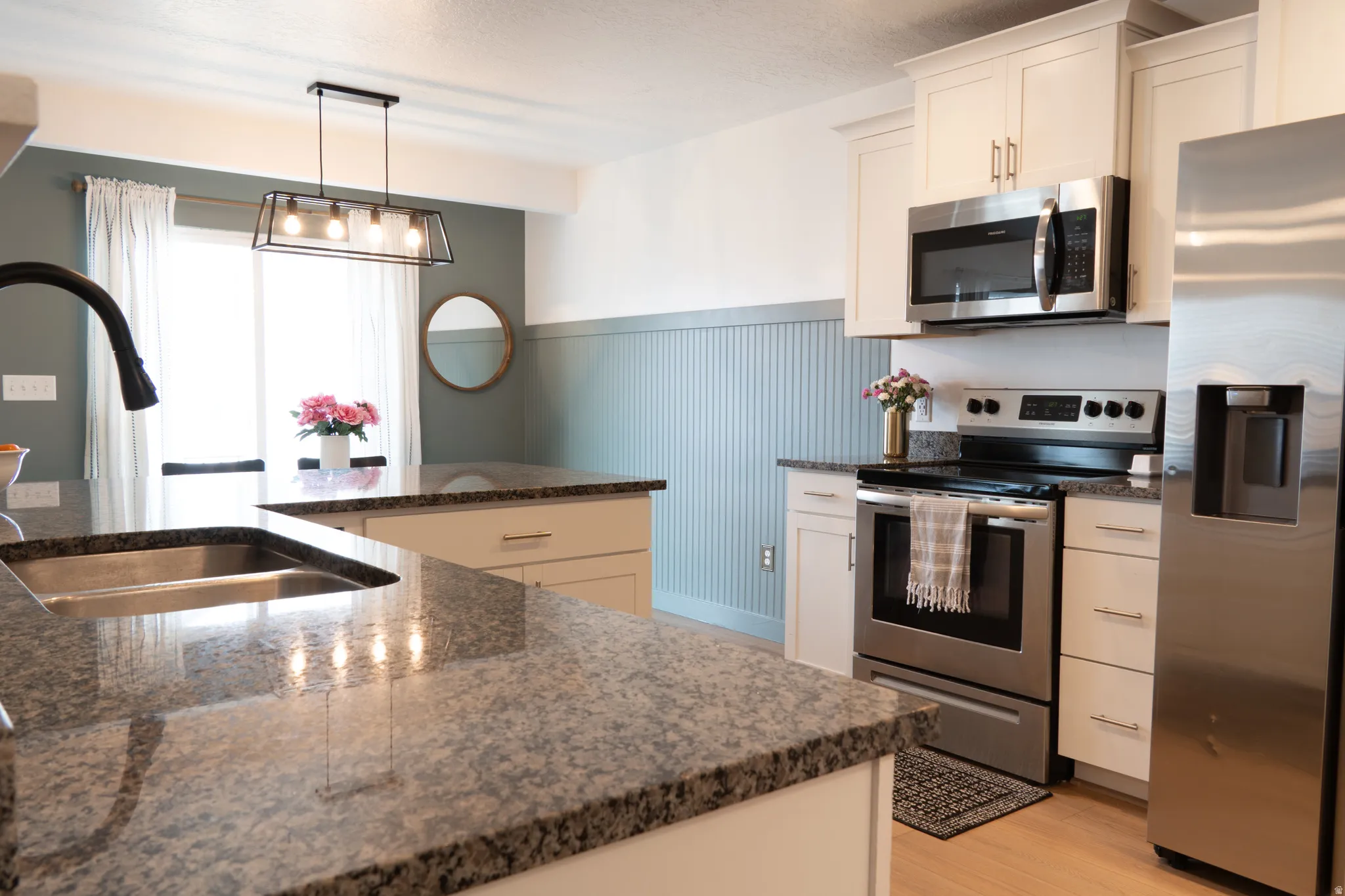 Kitchen with stainless steel appliances, wainscoting, white cabinets, decorative light fixtures, and dark stone counters