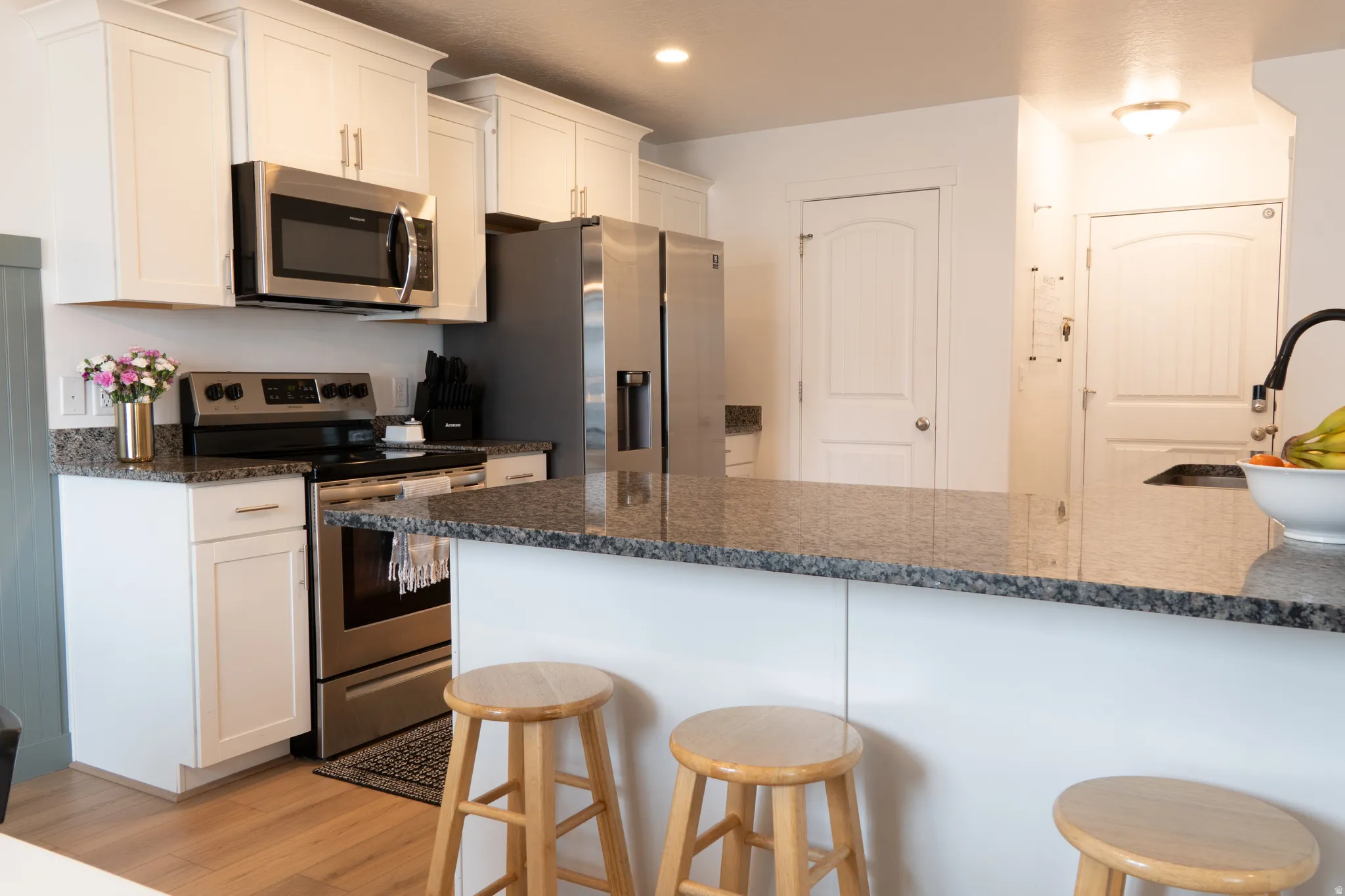 Kitchen featuring stainless steel appliances, a breakfast bar area, white cabinets, light wood-style floors, and dark stone counters