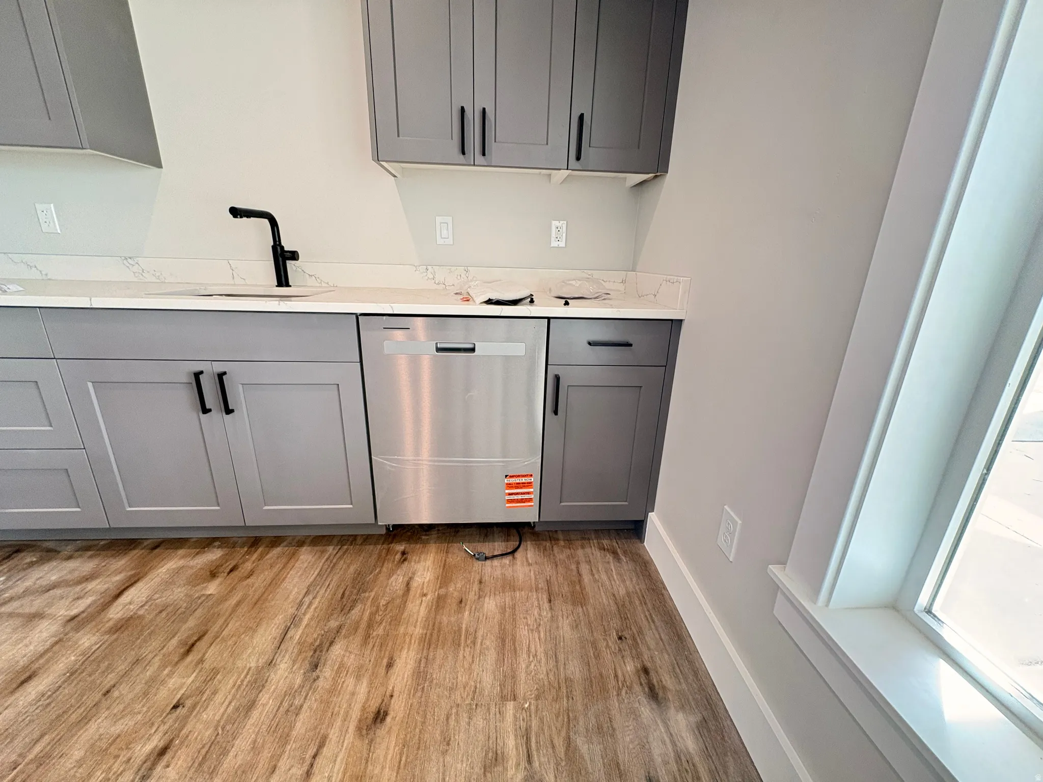 Bar area with gray cabinets, dishwasher, light wood-style flooring, and light stone counters