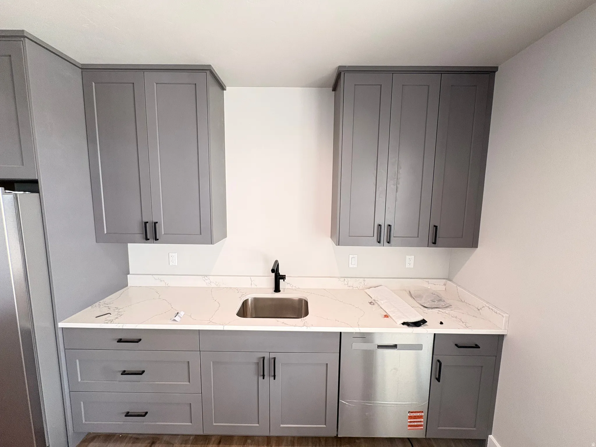 Kitchen with gray cabinetry, stainless steel appliances, light stone countertops, and wood finished floors