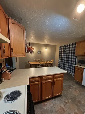 Kitchen with light countertops, white electric stove, a peninsula, wood finish cabinets, and stainless steel microwave