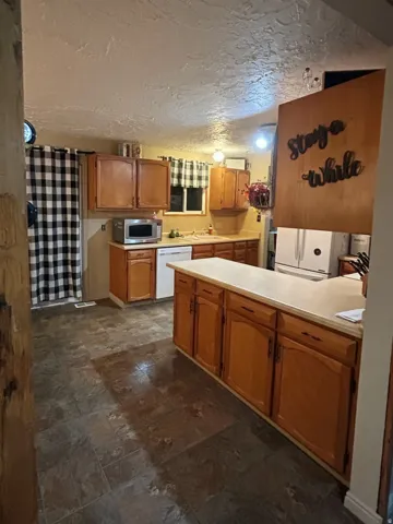 Kitchen with light countertops, white appliances, wood finish cabinetry, a peninsula, and a textured ceiling