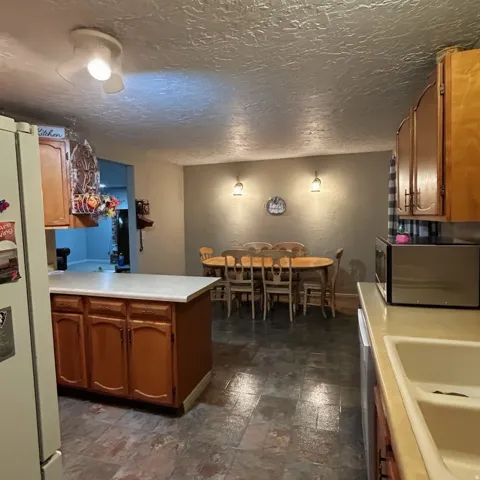 Kitchen with stainless steel microwave, freestanding refrigerator, light countertops, wood finish cabinetry, and a peninsula