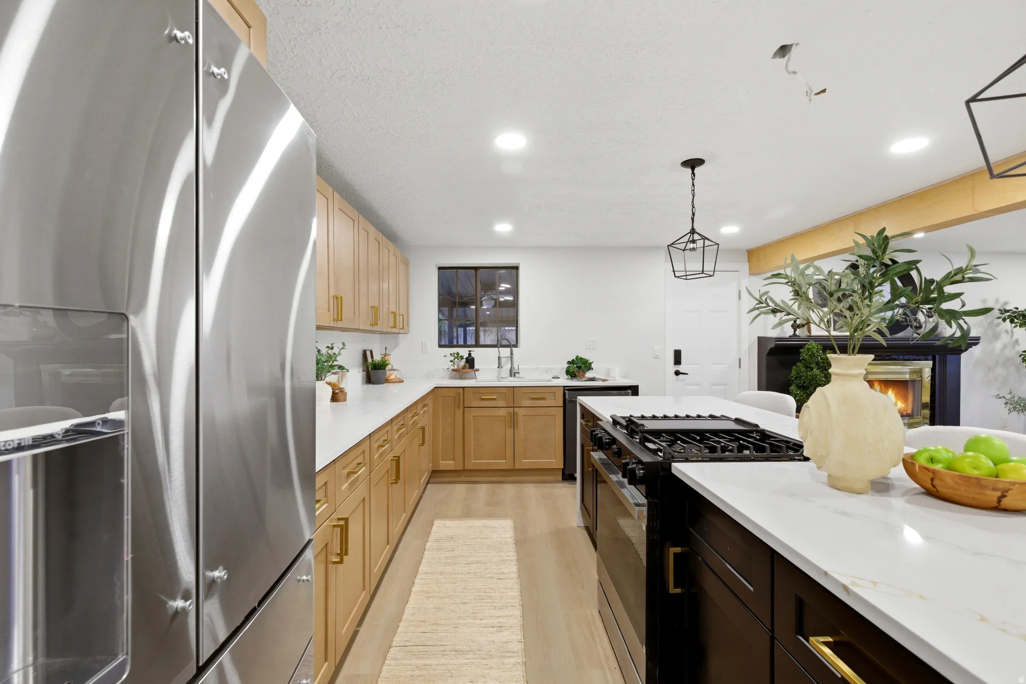 Dual tone kitchen featuring stainless steel fridge with ice dispenser, black range with gas stovetop, light stone countertops, two tone cabinets, and decorative light fixtures