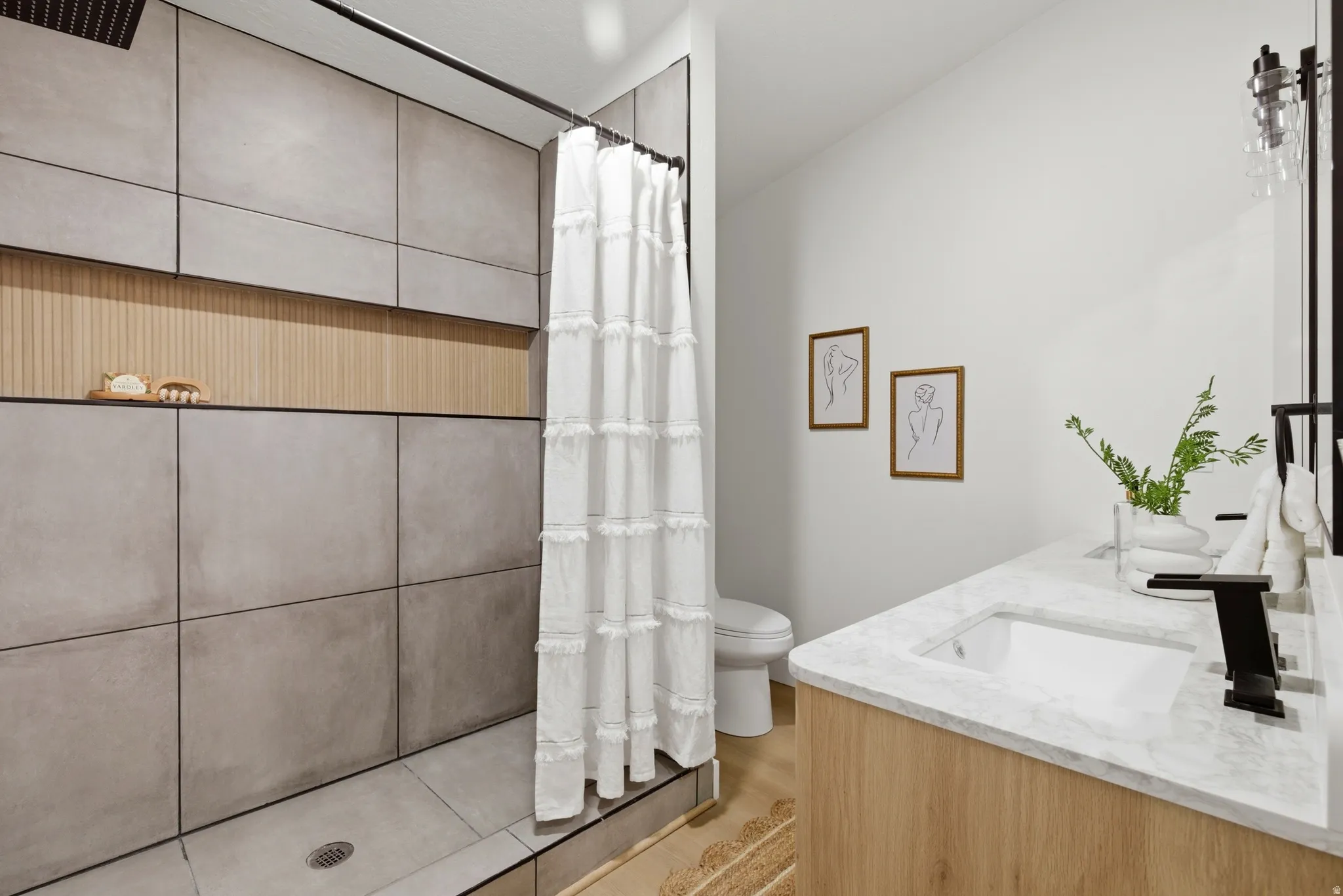 Bathroom with tiled shower, double vanity, and light wood-style flooring