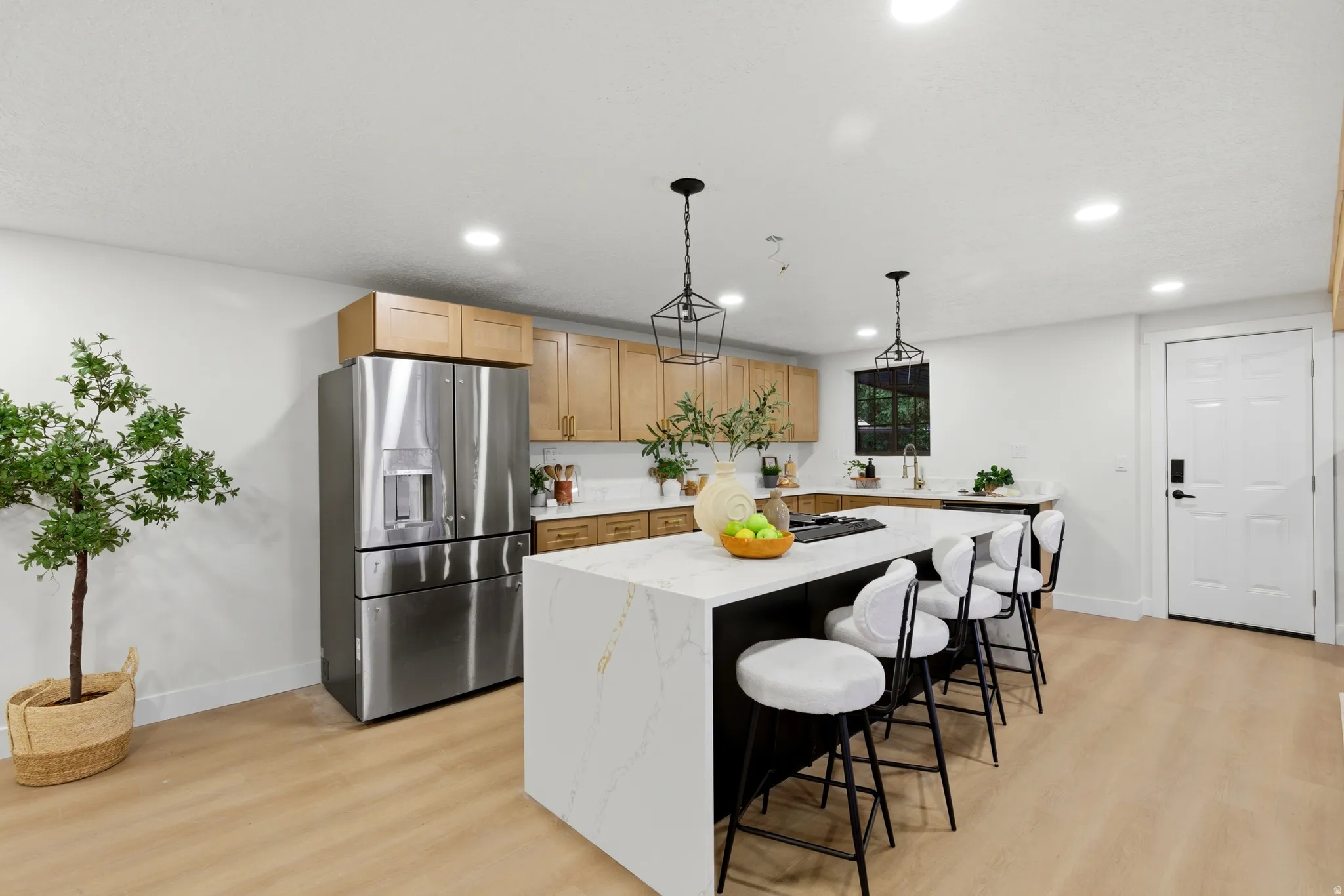 Kitchen with stainless steel fridge with ice dispenser, decorative light fixtures, light wood-style floors, and light wood finish cabinets